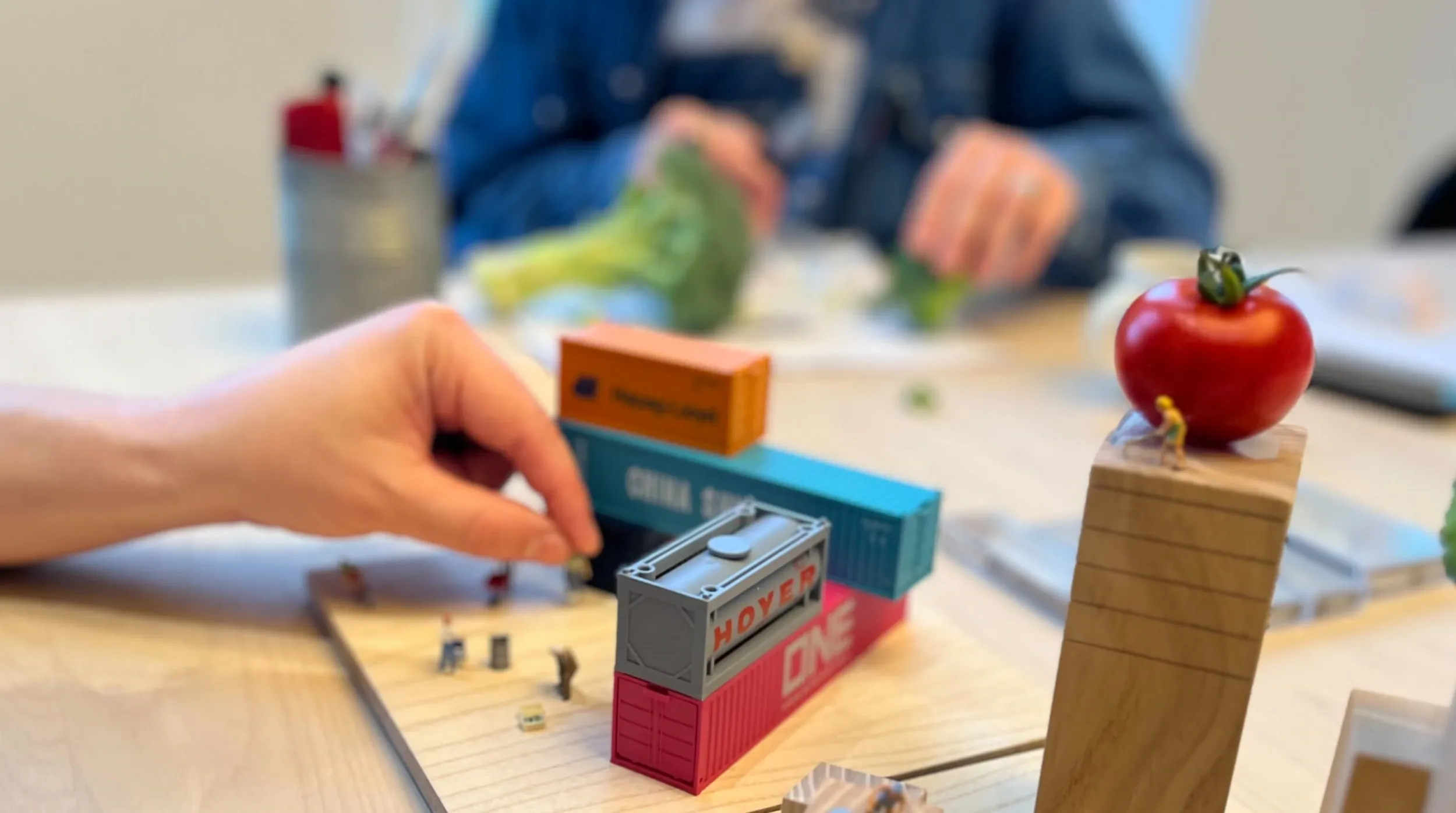 A hand placing miniture people amongst miniature containers